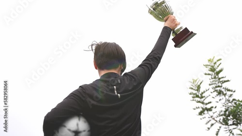 Back turned teenage soccer player footballer boy lifting the trophy to the sky. Winner success championship. photo