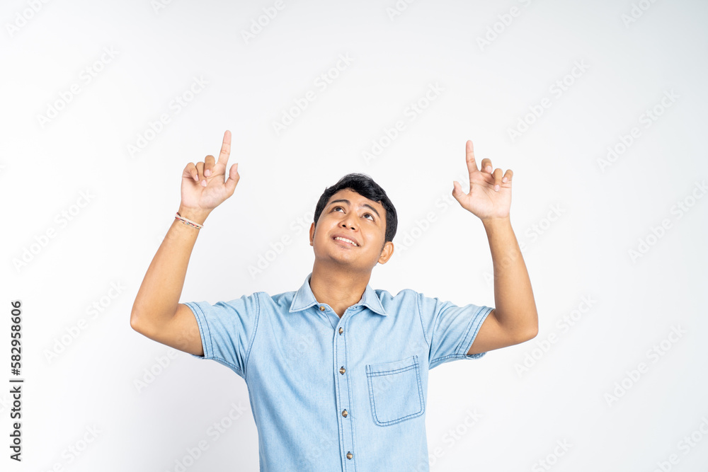 portrait of a young Asian man standing with both fingers pointing and looking up against an isolated background portrait of a young Asian man standing with both fingers pointing and looking up against an isolated background