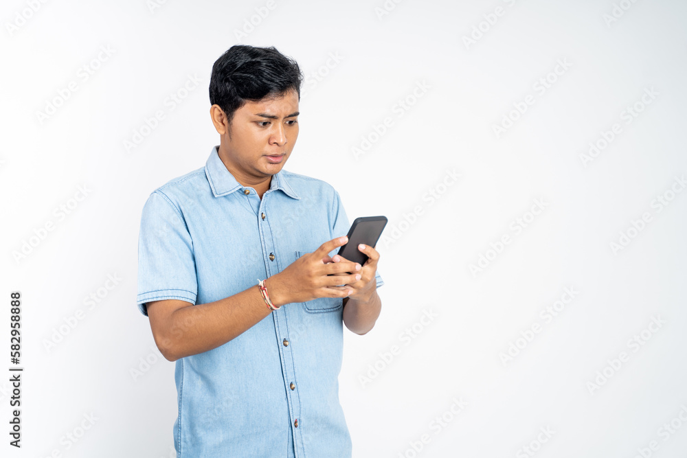 portrait of young Asian man shocked watching video using cell phone on isolated background portrait of young Asian man shocked watching video using cell phone on isolated background