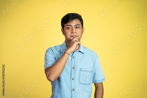 young asian man stand with sardonic expression as hand on chin in isolated background
