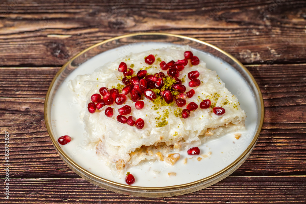 Gullac dessert. Ramadan dessert. Gullac garnished with pomegranate and pistachio in glass plate on wood background. Symbolic food.