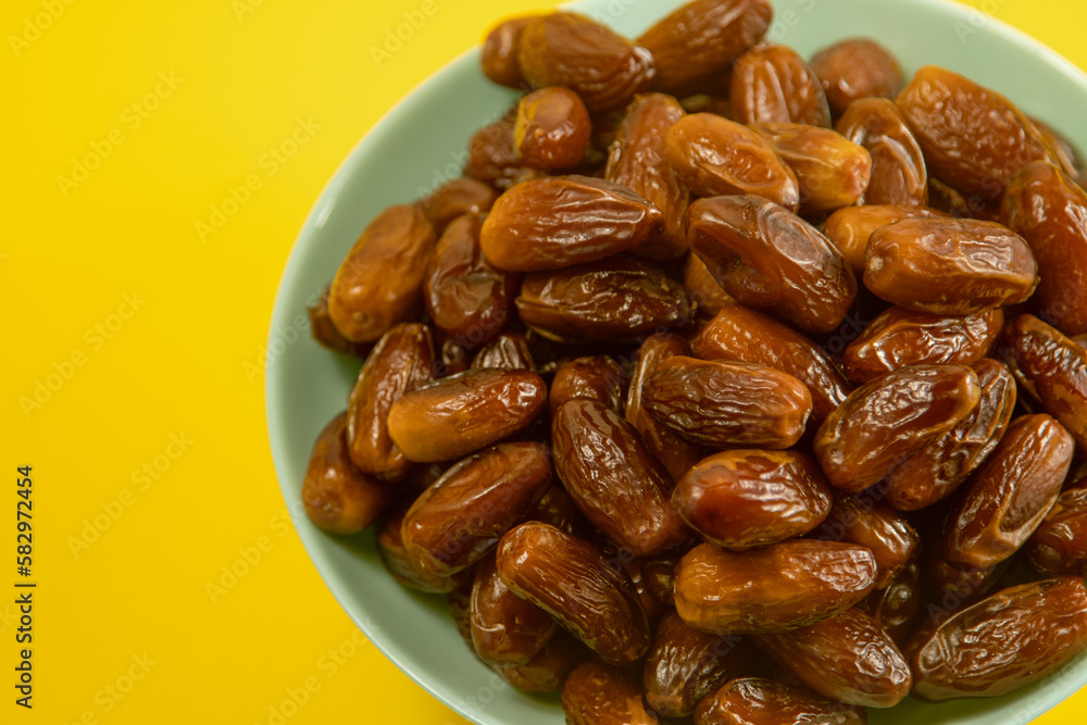 Dates. Dried date palm fruits. Healthy sweet snack food bowl. Pile of tasty dry dattes in plate. Date harvest symbolizing Ramadan. Blue plate on yellow background Dates. Dried date palm fruits. Healthy sweet snack food bowl. Pile of tasty dry dattes in plate. Date harvest symbolizing Ramadan. Blue plate on yellow background