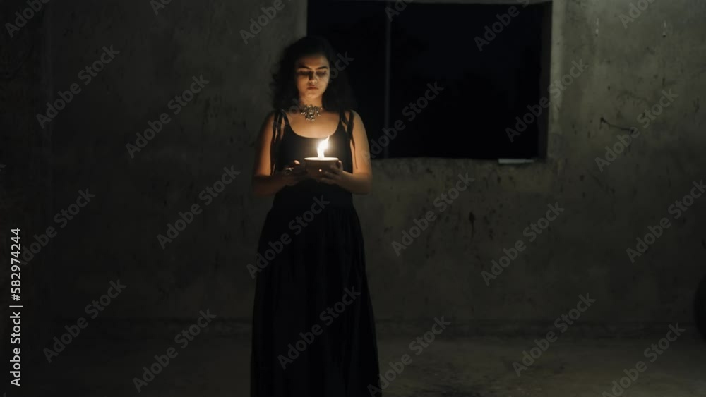 Front view of woman in black dress with long hair, moving in a dark room, drops a lighted candle from her hands. Front view of woman in black dress with long hair, moving in a dark room, drops a lighted candle from her hands.