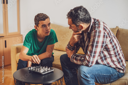 Father and son are playing chess at home.