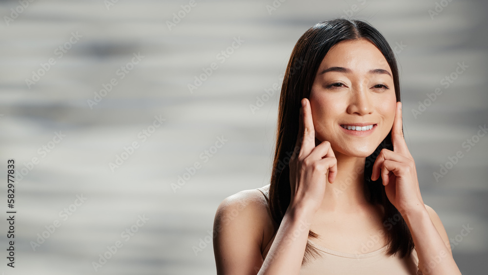 Flawless woman doing beauty routine with facial cream, applying moisturizer on face and advertising skincare cosmetics. Asian female model using sunscreen and promoting self confidence. Flawless woman doing beauty routine with facial cream, applying moisturizer on face and advertising skincare cosmetics. Asian female model using sunscreen and promoting self confidence.