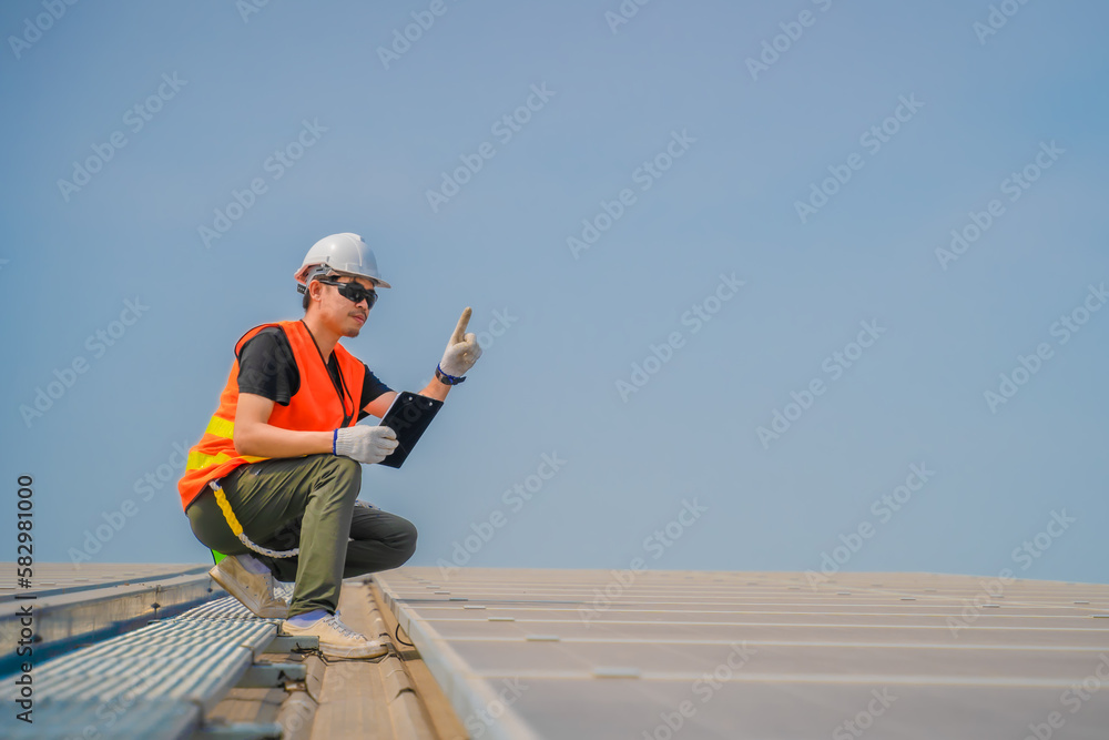 Asian engineer wearing protective vest and white hardhat sitting inspecting solar panel installation, Photovoltaic technology concept. Asian engineer wearing protective vest and white hardhat sitting inspecting solar panel installation, Photovoltaic technology concept.