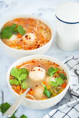 Potato balls soup with noodles and vegetables in white bowl, white background. Vegan food concept.