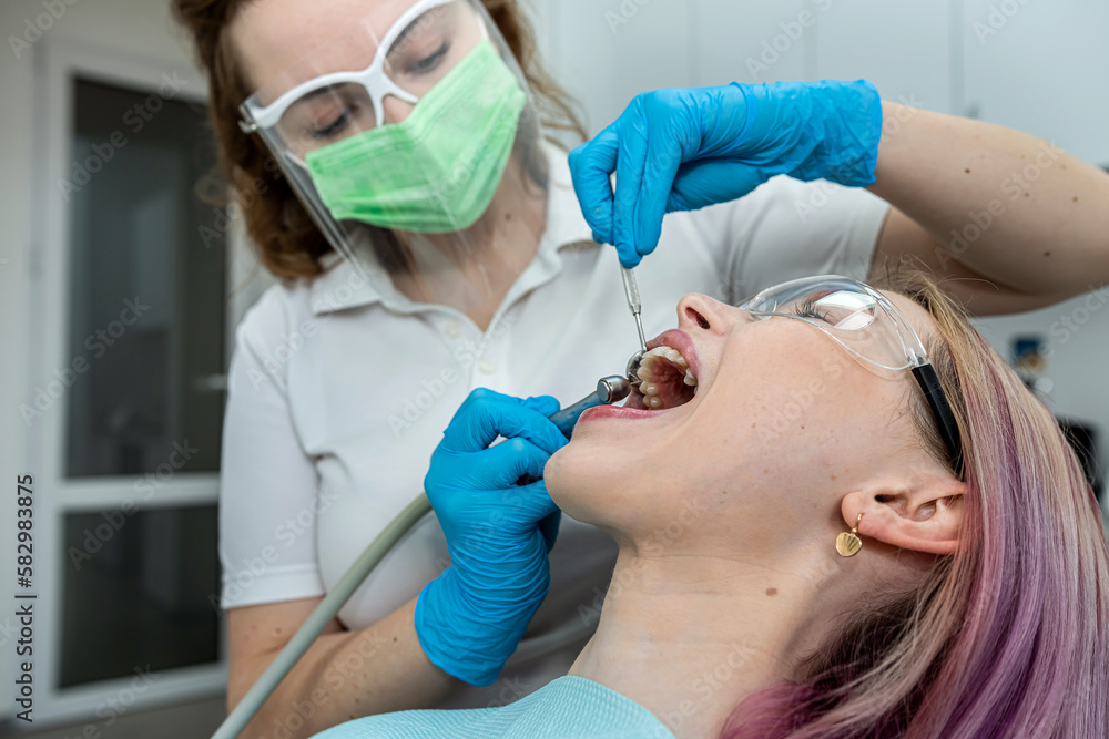 woman is sitting in medical chair while female dentist is fixing her teeth in a dental clinic. woman is sitting in medical chair while female dentist is fixing her teeth in a dental clinic.