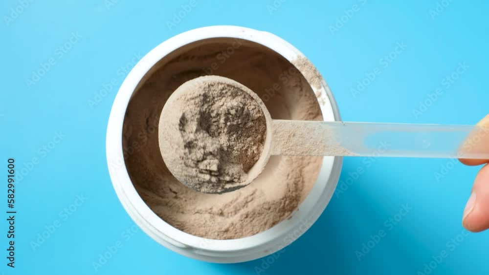 Female hand takes out protein powder in scoop from a jar on a blue background top view. Female hand takes out protein powder in scoop from a jar on a blue background top view.