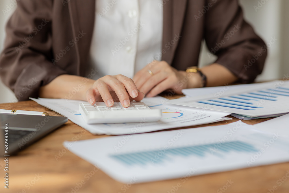 Close-up shot of businesswoman using calculator and laptop to calculate company financial result On wooden table in office and business background, tax, accounting, statistics and analytical research. Close-up shot of businesswoman using calculator and laptop to calculate company financial result On wooden table in office and business background, tax, accounting, statistics and analytical research.