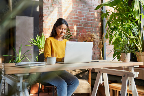 Businesswoman using laptop at desk amidst plants at loft office
