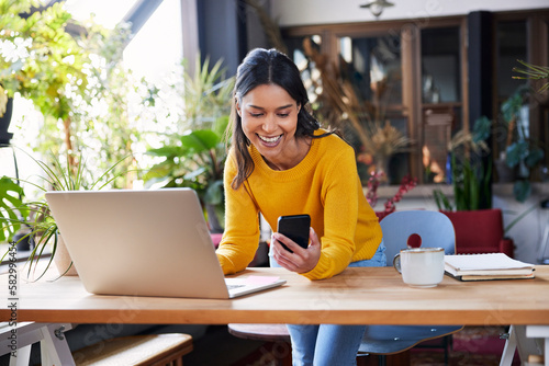 Smiling businesswoman using mobile phone leaning on desk at loft office