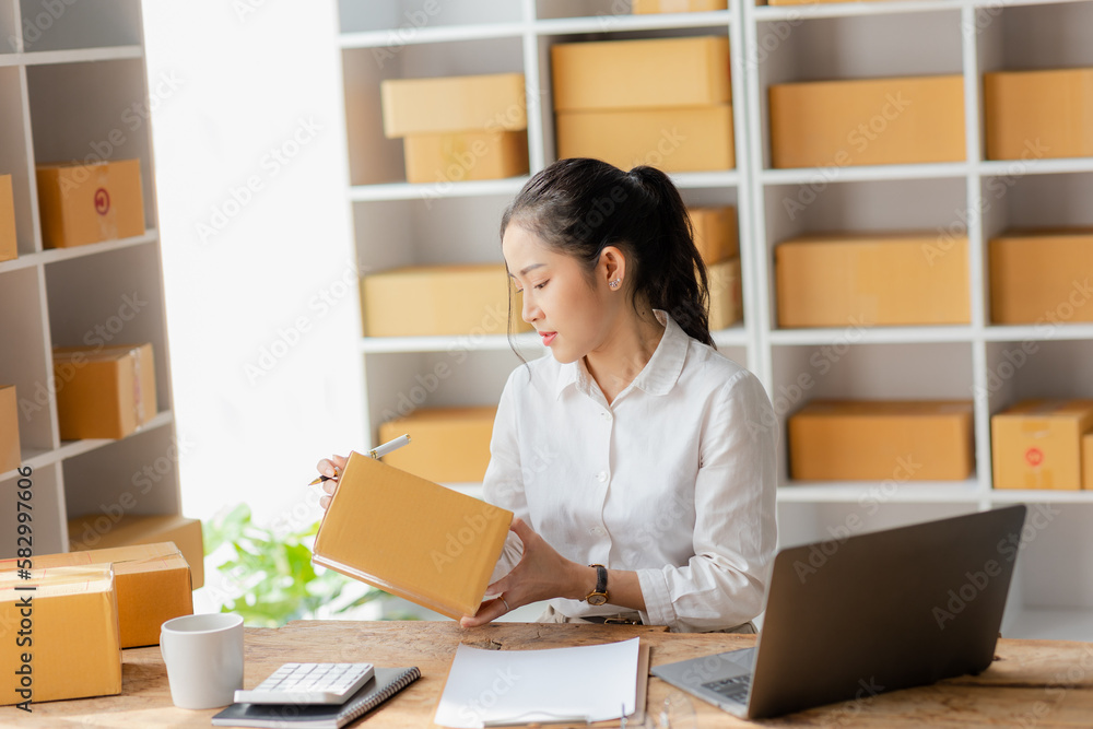 Online shopping, beautiful smiling asian woman checking order and customer details and address on laptop or box to prepare delivery accordingly, SME online shopping Online shopping, beautiful smiling asian woman checking order and customer details and address on laptop or box to prepare delivery accordingly, SME online shopping
