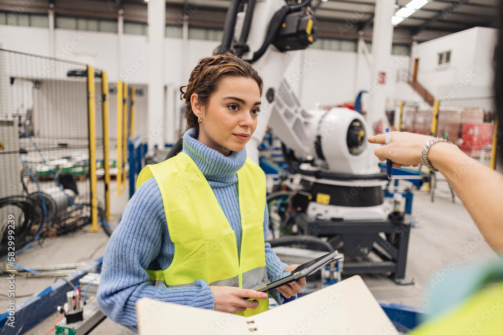 Engineer gesturing colleague with tablet PC in robotics factory Engineer gesturing colleague with tablet PC in robotics factory