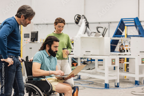 Engineer sitting in wheelchair discussing with colleagues on laptop in factory