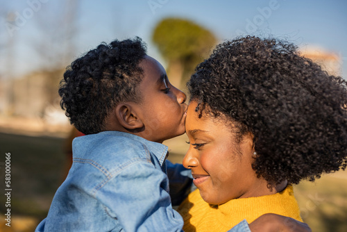 Boy kissing forehead of mother in park photo