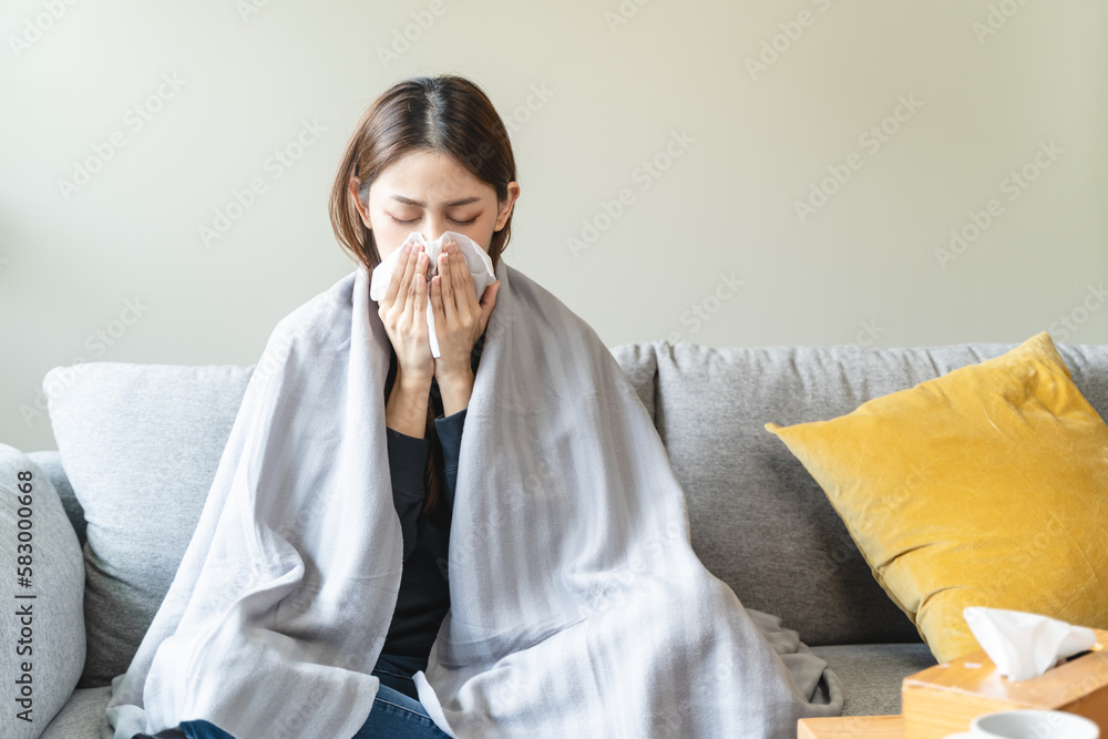 © Pormezz - Sick at home concept. Woman sneezing on the sofa in winter season.