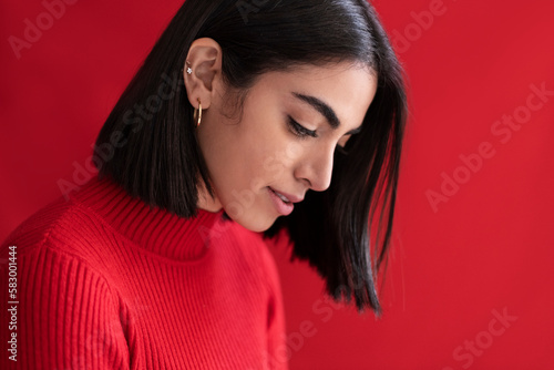 Shy young woman looking down against red background