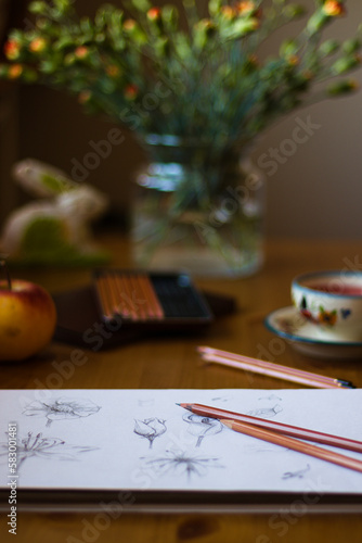szkicownik na stole, filiżanka jabłko i kwiaty w parcowni