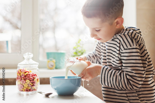 Boy pouring milk in bowl on table at home photo