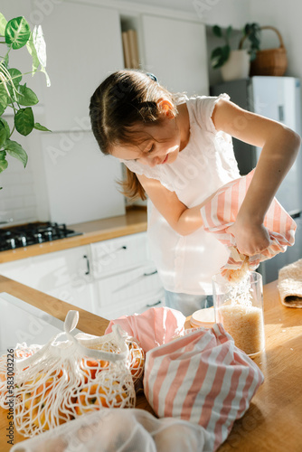 Girl pouring rice from reusable bag in glass jar at home photo