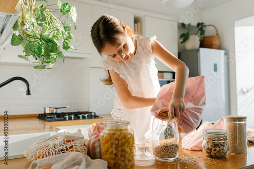 Girl pouring oat meal from reusable bag in glass jar photo