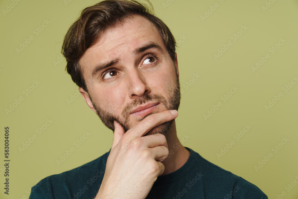 Pensive man touching his chin and looking away isolated over green wall