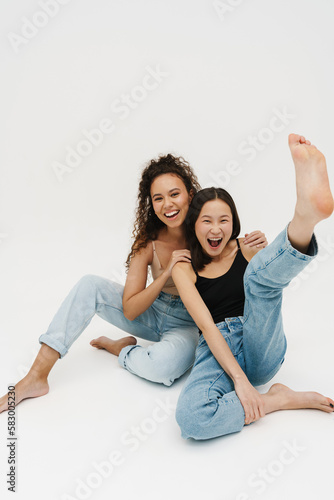Two girls having fun together while sitting isolated over white wall