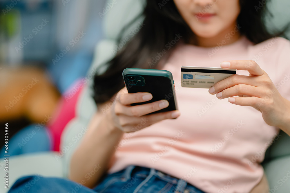 Young beautiful asian woman relaxing on sofa at home using mobile phone and credit card for online shopping Activities on vacation