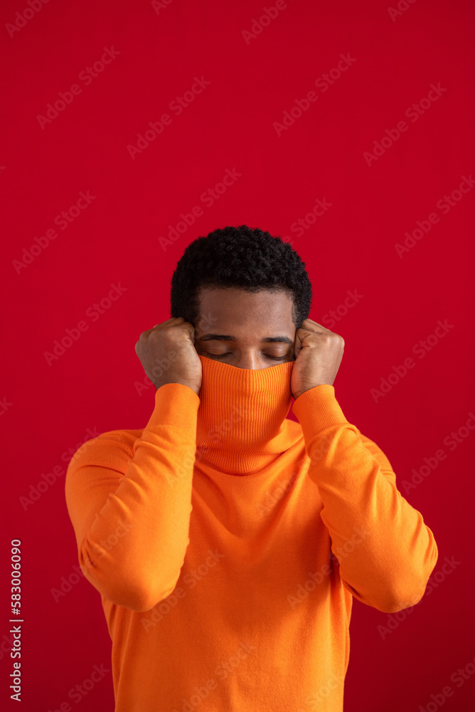 Man covering face with turtleneck sweater against red background Man covering face with turtleneck sweater against red background
