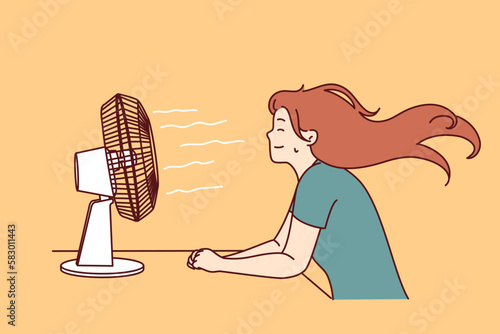 Woman sitting in front of fan enjoying cold wind after walking in hot summer weather or doing housework. Sweaty girl cools herself using electric fan due to sudden warming and climate change 