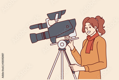 Woman videographer stands near professional video camera fixed on tripod and shoots film or news report. Girl working as producer or director in film studio uses modern filming equipment