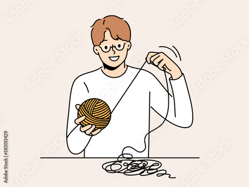 Smiling man sit at table with thread in hands. Happy male in glasses weaving or yarning. Hobby and leisure activity. Vector illustration. 