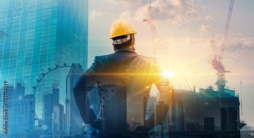 Quadro su tela Engineer wearing yellow helmet for workers security  of new highrise apartment buildings and construction cranes on evening sunset
