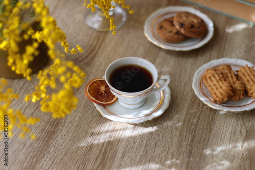 Cup of tea, plates with cookies, glass of orange juice, books, reading glasses, bowl of fruit and candles on the table. Selective focus.
