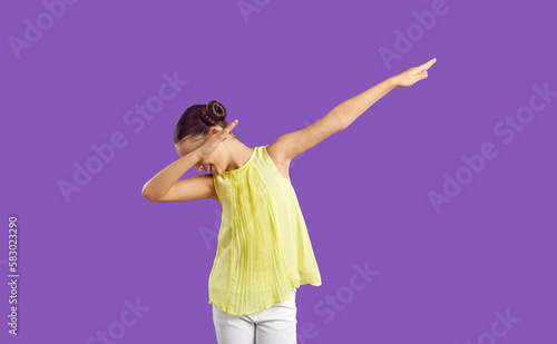 Happy child dabbing. Cheerful kid having fun in studio. Little girl with hair buns standing isolated on purple color background, doing funny dub gesture and smiling. Victory, success, hype concept
