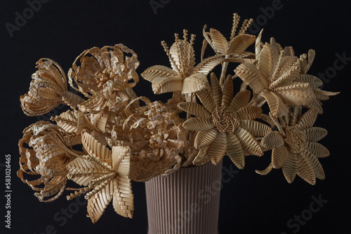 The flowers is made of straw on a dark background in a cardboard vase