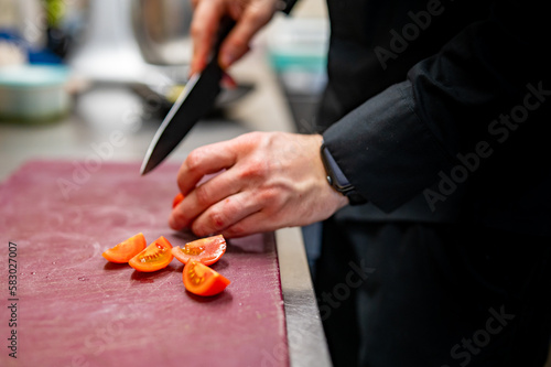Chef hand cut tomatoes on a chopping board in kitchen