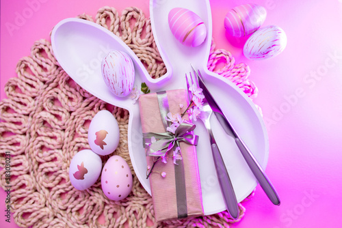 Canvas Print bunny plate with cutlery , easter eggs, gifts with green ribbon, spring sakura flowers on a pastel pink background with neon glow