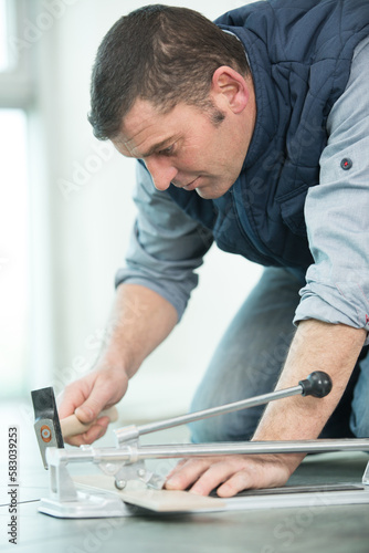 mature tiler tapping scored tile apart with hammer