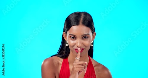 Secret, face and woman with finger on lips in studio, blue background and privacy sign. Portrait of indian model, silence and shush for quiet, gossip and whisper of confidential mystery, emoji or photo