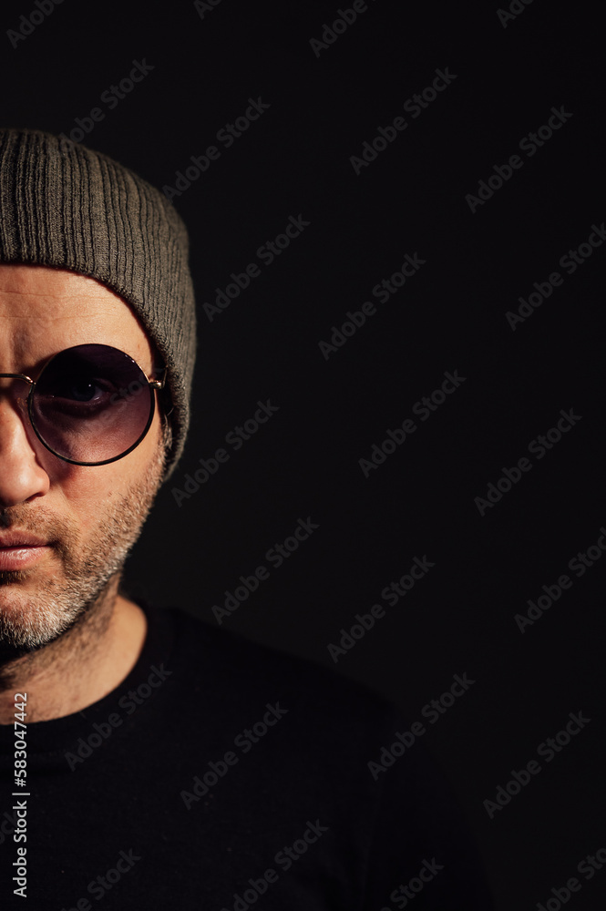 Serious dramatic man in sunglasses looking away while standing against black studio background Serious dramatic man in sunglasses looking away while standing against black studio background