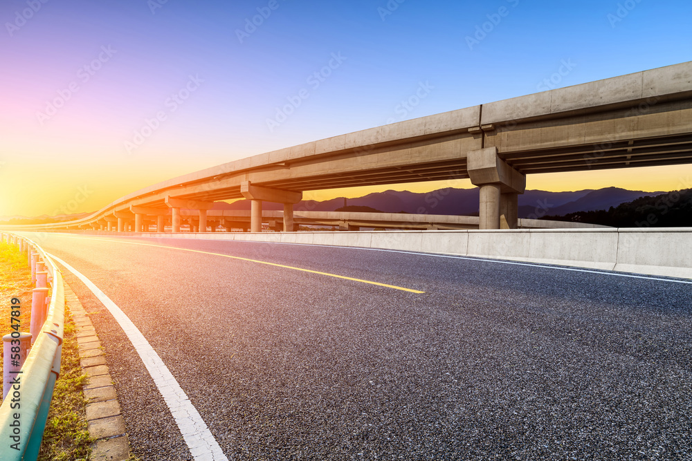 Asphalt road and bridge with mountain background at sunset