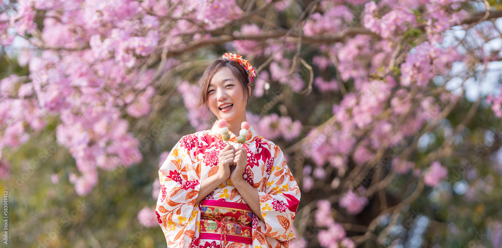 Japanese woman in traditional kimono dress holding sweet hanami dango dessert while walking in the park at cherry blossom tree during spring sakura festival with copy space Japanese woman in traditional kimono dress holding sweet hanami dango dessert while walking in the park at cherry blossom tree during spring sakura festival with copy space