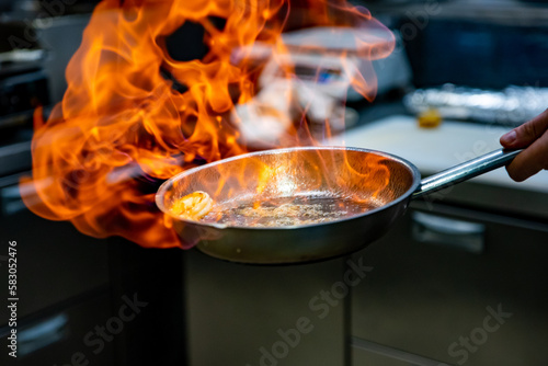 Chef hand in restaurant kitchen with pan, cooking flambe on shrimps