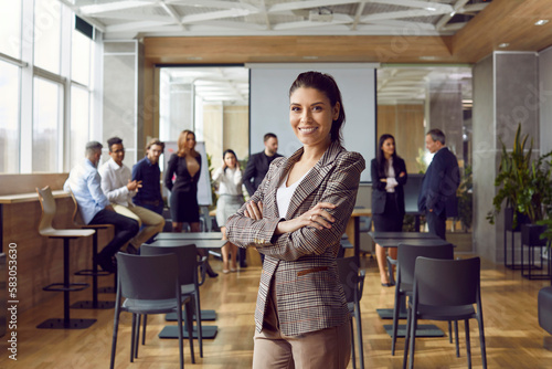 Happy professional business teacher after corporate training class for team of workers. Beautiful young woman in suit jacket standing in office conference room, looking at camera and smiling photo