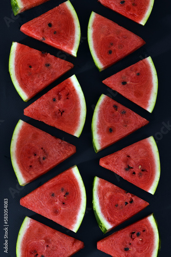 A pattern of watermelon slices. Cut pieces of red ripe delicious juicy watermelon on a black background