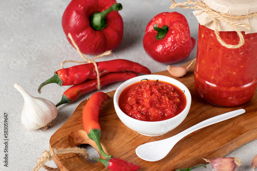 Traditional sauce adjika with hot chili pepper, paste harissa in white bowl on wooden board, Closeup photo