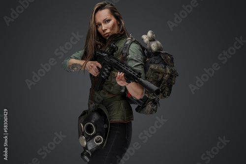 Studio shot of female mercenary carrying backpack and holding rifle. photo