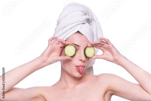 Beautiful woman with clean fresh skin makes tongue applying cream with two cocumbers on eyes. Gherkin care treatment. Natural healthy cosmetic funny portrait. Cosmetology, beauty, spa